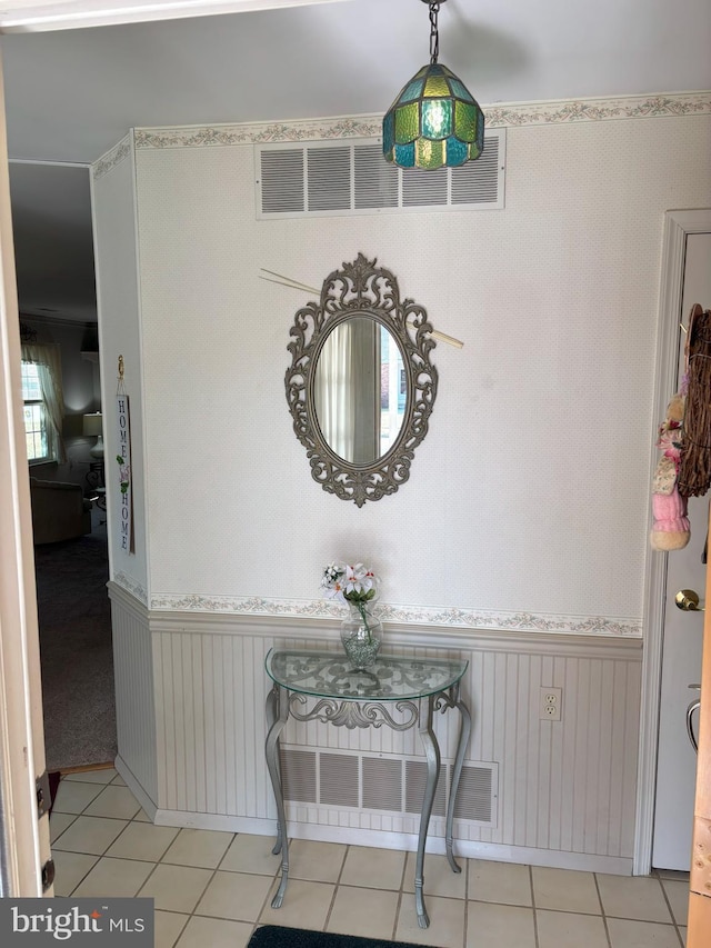 hallway with a wainscoted wall, light tile patterned floors, and visible vents