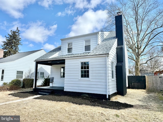 rear view of house featuring covered porch, roof with shingles, fence, and a chimney