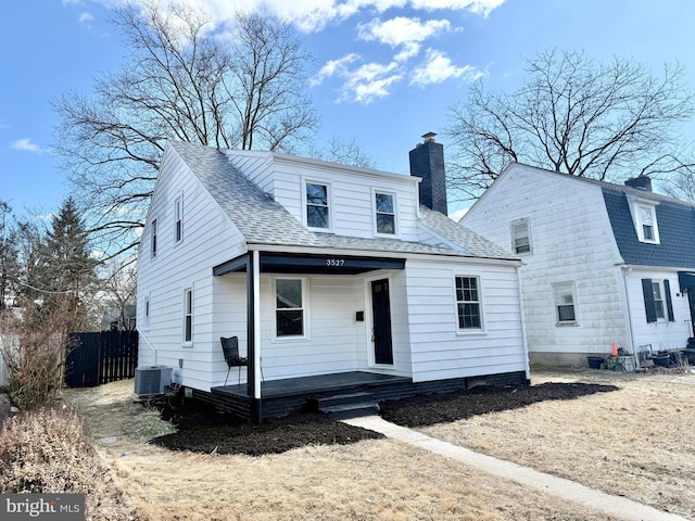 view of front facade with a porch, central AC unit, a shingled roof, fence, and a chimney