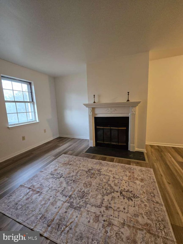 unfurnished living room featuring a fireplace with flush hearth, dark wood finished floors, a textured ceiling, and baseboards