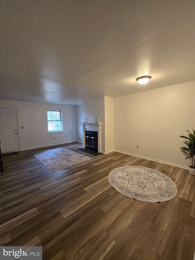 unfurnished living room with dark wood-style flooring, a fireplace with flush hearth, and baseboards