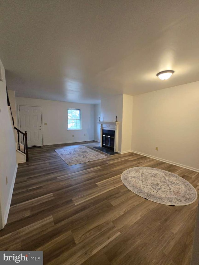 unfurnished living room with dark wood-type flooring, baseboards, stairway, and a fireplace with flush hearth