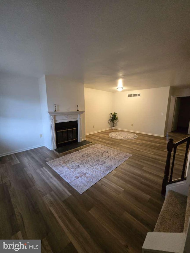 unfurnished living room with a fireplace with flush hearth, baseboards, visible vents, and dark wood-type flooring