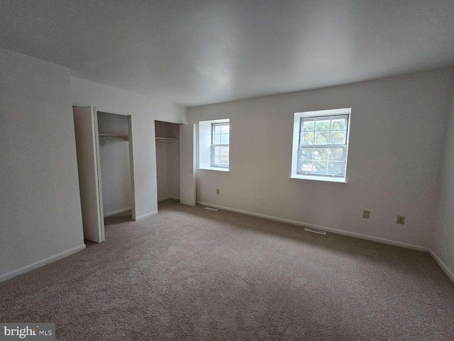 unfurnished bedroom featuring baseboards, carpet floors, visible vents, and multiple closets