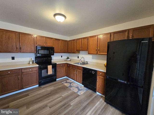 kitchen featuring light wood-style floors, light countertops, a sink, and black appliances