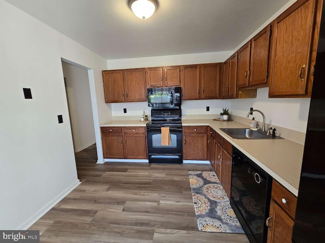 kitchen featuring brown cabinetry, wood finished floors, light countertops, black appliances, and a sink