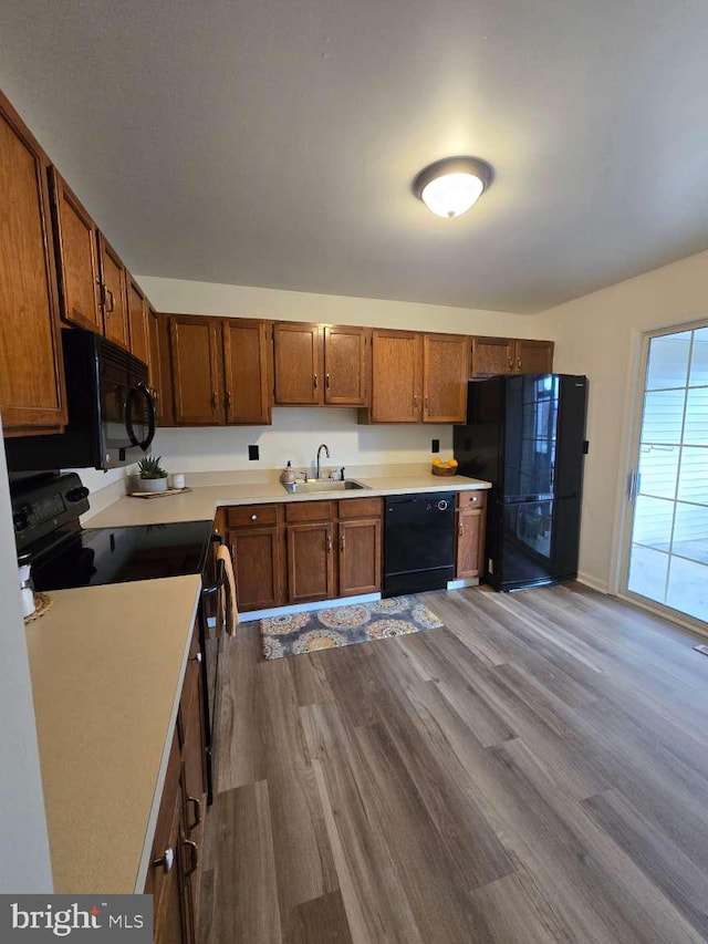 kitchen featuring a sink, light countertops, light wood-type flooring, black appliances, and brown cabinetry