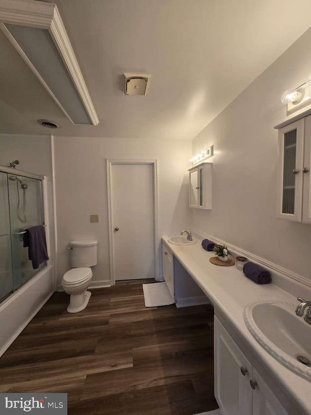 full bath with wood finished floors, double vanity, combined bath / shower with glass door, and a sink