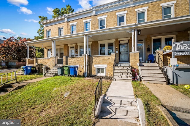 view of property with covered porch, brick siding, and a front lawn