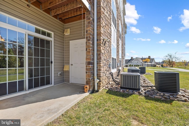 doorway to property with stone siding, central AC, and a yard