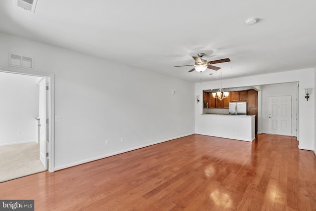 unfurnished living room featuring ceiling fan with notable chandelier, visible vents, light wood finished floors, and baseboards