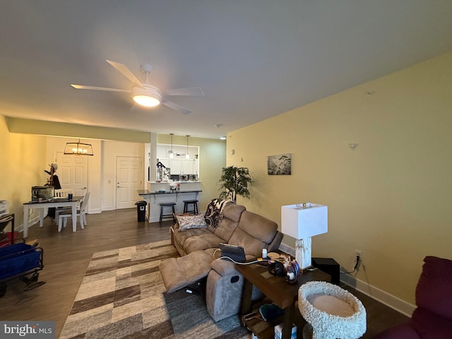 living room with dark wood-style floors, baseboards, and ceiling fan with notable chandelier