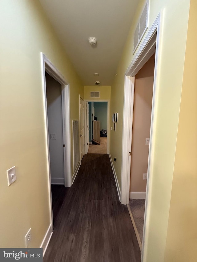 hall with dark wood-style floors, visible vents, and baseboards