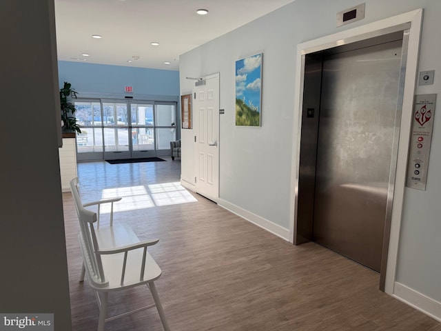 corridor featuring recessed lighting, elevator, baseboards, and wood finished floors