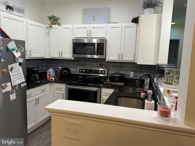 kitchen with tasteful backsplash, appliances with stainless steel finishes, white cabinetry, a sink, and a peninsula