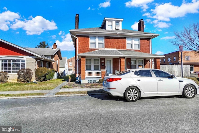 american foursquare style home featuring a chimney, fence, a porch, and brick siding