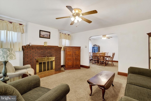 living room with arched walkways, light colored carpet, a ceiling fan, baseboards, and a brick fireplace