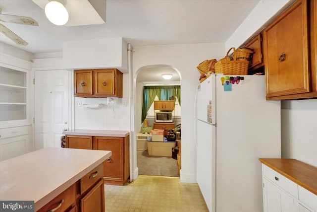 kitchen featuring light floors, light countertops, brown cabinetry, freestanding refrigerator, and a ceiling fan