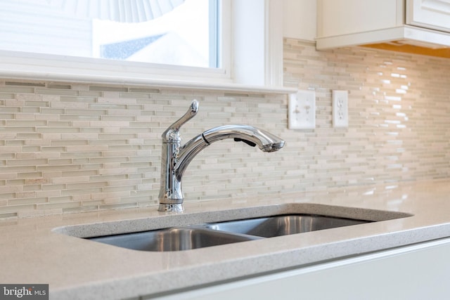 room details featuring white cabinetry, a sink, decorative backsplash, and light stone countertops