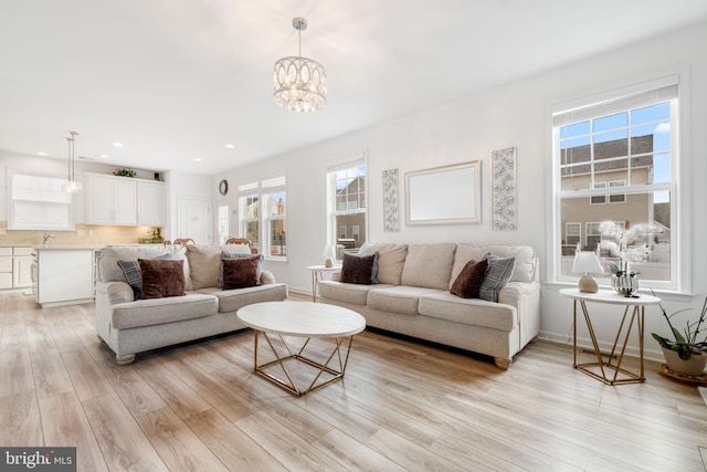 living area featuring light wood-type flooring, a notable chandelier, baseboards, and recessed lighting