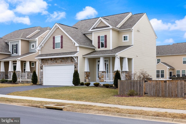 craftsman inspired home featuring aphalt driveway, covered porch, fence, a garage, and a front lawn