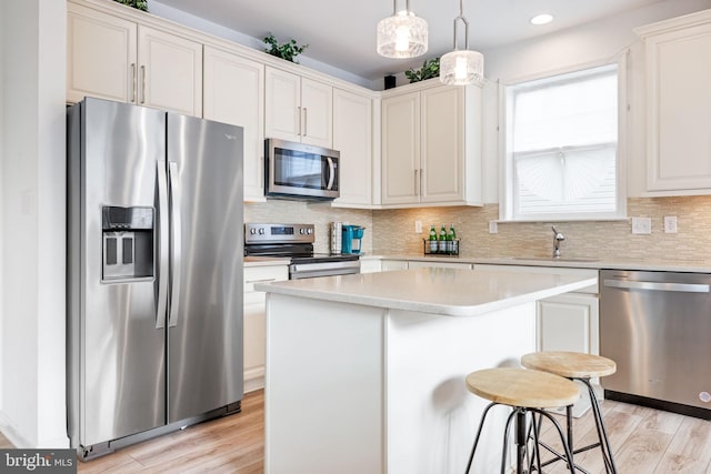 kitchen featuring light countertops, decorative backsplash, appliances with stainless steel finishes, a sink, and light wood-type flooring