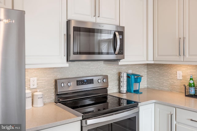 kitchen with stainless steel appliances, light countertops, white cabinetry, and decorative backsplash