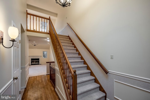 staircase with wood-type flooring, a fireplace, and a high ceiling