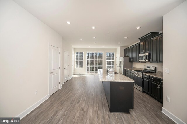 kitchen featuring a kitchen island with sink, dark wood-style flooring, stainless steel appliances, and a sink