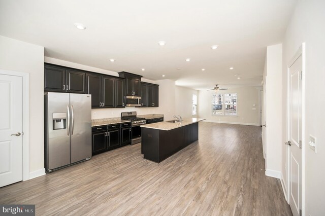 kitchen featuring light wood finished floors, appliances with stainless steel finishes, a sink, and a center island with sink