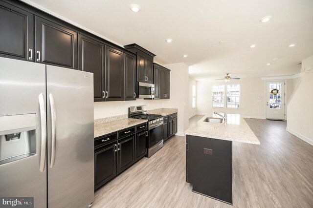 kitchen featuring light wood finished floors, appliances with stainless steel finishes, a sink, and dark cabinetry