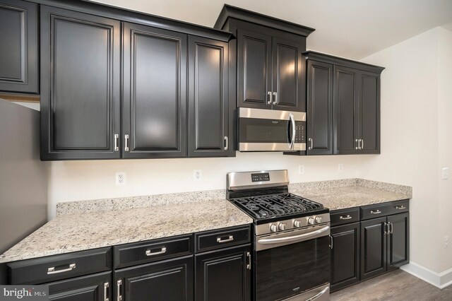 kitchen with stainless steel appliances, light wood-type flooring, dark cabinets, and baseboards