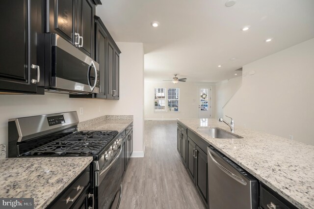 kitchen with dark cabinets, light wood-style floors, stainless steel appliances, and a sink