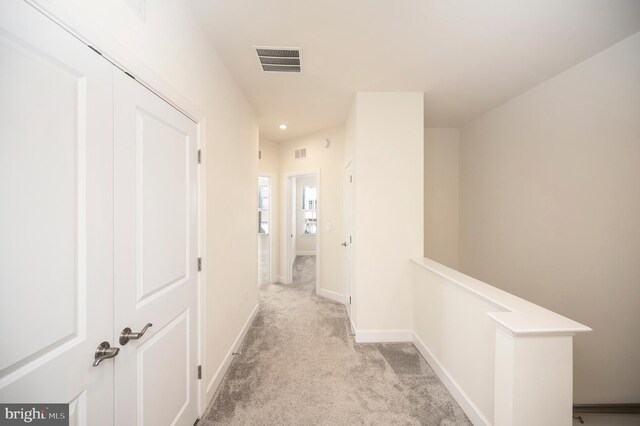 hallway featuring baseboards, visible vents, light carpet, and an upstairs landing