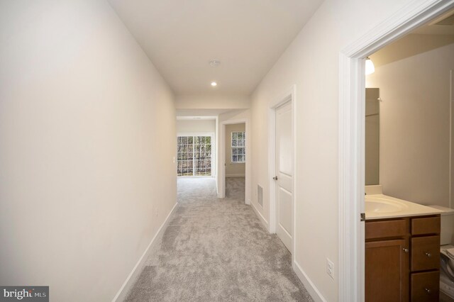 corridor featuring light carpet, visible vents, baseboards, and a sink