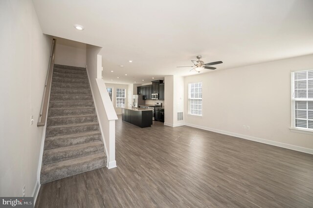 unfurnished living room featuring a healthy amount of sunlight, dark wood-style floors, stairs, and baseboards