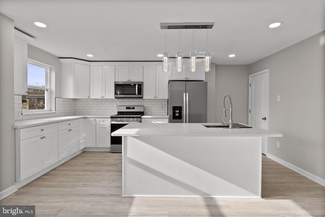 kitchen featuring white cabinets, appliances with stainless steel finishes, decorative light fixtures, a kitchen island with sink, and a sink