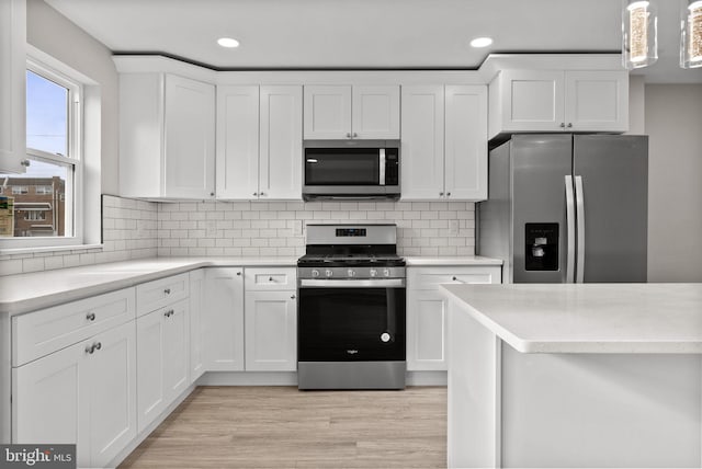 kitchen featuring stainless steel appliances, tasteful backsplash, light countertops, hanging light fixtures, and white cabinets