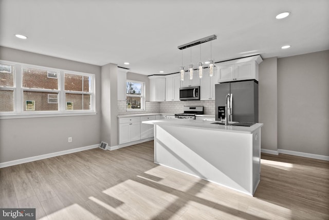 kitchen featuring a kitchen island, white cabinets, appliances with stainless steel finishes, light wood finished floors, and decorative light fixtures