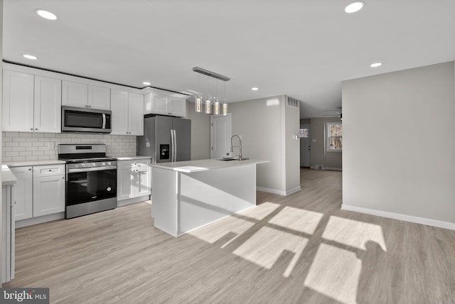 kitchen featuring stainless steel appliances, a sink, white cabinetry, light countertops, and decorative light fixtures