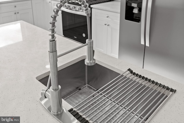 interior details with light stone countertops, stainless steel appliances, white cabinets, and a sink