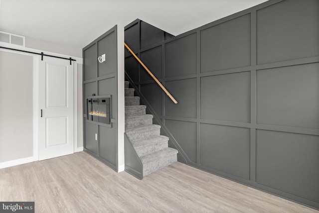 stairs featuring wood finished floors, visible vents, a decorative wall, and a barn door