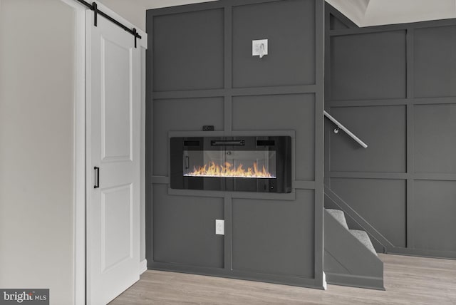 room details featuring a glass covered fireplace, wood finished floors, a decorative wall, and a barn door