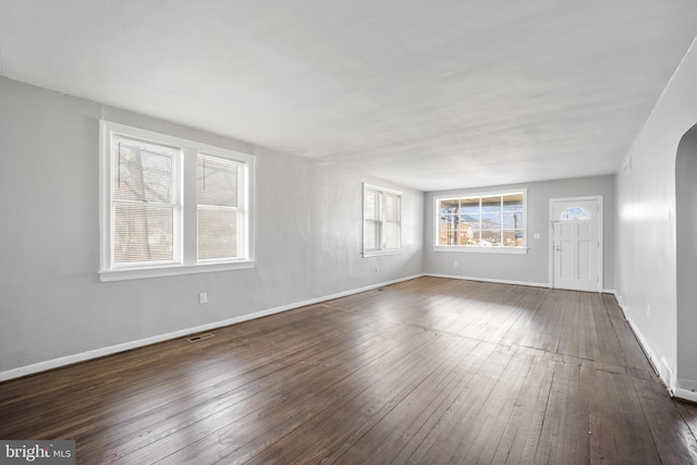 unfurnished living room featuring dark wood-style floors, arched walkways, visible vents, and baseboards