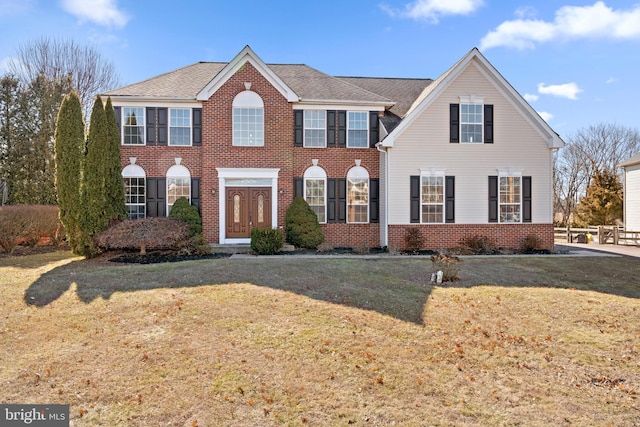 view of front of house with a shingled roof, a front yard, and brick siding