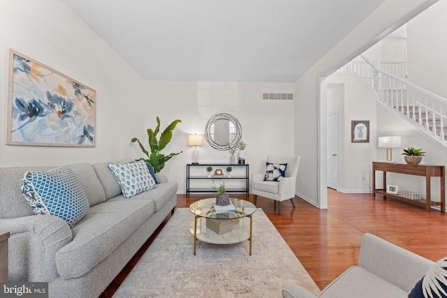 living room with stairway, baseboards, visible vents, and wood finished floors