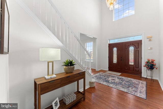 entryway with baseboards, wood finished floors, an inviting chandelier, stairs, and a high ceiling