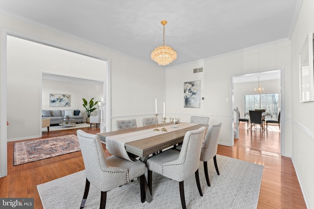 dining area with a chandelier, light wood-type flooring, visible vents, and ornamental molding