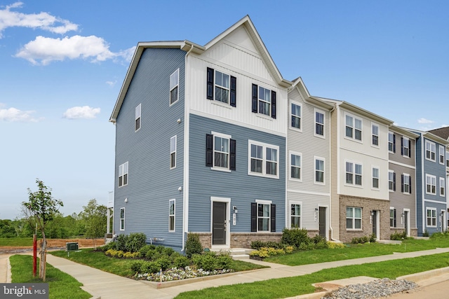 townhome / multi-family property featuring central AC unit, brick siding, board and batten siding, and a front yard