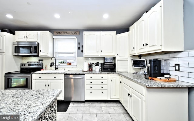 kitchen featuring tasteful backsplash, white cabinets, light stone counters, stainless steel appliances, and a sink